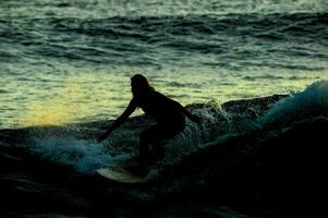 uma surfista passeios uma onda às pôr do sol foto