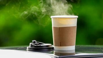 café Leve embora dentro uma papel copo em topo do a carro cobertura verde árvore fundo às nascer do sol dentro a manhã, seletivo foco, suave foco. foto