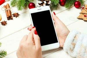 vista superior de uma mulher segurando um telefone na mão no fundo de madeira do ano novo feito de abeto e decorações festivas. conceito de férias de natal. brincar foto