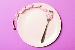 conceito de dieta estrita com espaço vazio para o seu design. vista superior do prato com garfo na fita métrica no fundo roxo foto
