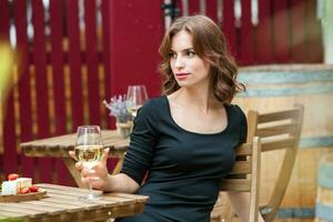 lindo jovem mulher bebendo branco vinho em a terraço do uma restaurante. relaxante depois de trabalhos com uma vidro do vinho. solteiro mulher tendo Diversão. foto