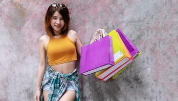 atraente alegre animado jovem mulher segurando colorida compras bolsas em concreto paredes fundo com cópia de espaço. felicidade, consumidor, venda e pessoas conceito. foto