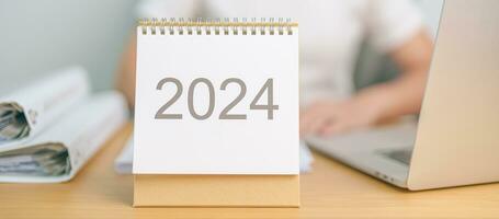 2024 ano calendário em mesa com o negócio mulher usando computador portátil computador. contagem regressiva, feliz Novo ano, resolução, metas, plano, Ação, missão e financeiro conceito foto