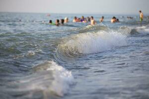 mar onda em a fundo do borrado pessoas natação dentro a mar. foto