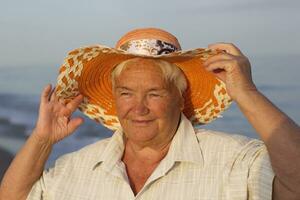 lindo idosos mulher dentro uma chapéu em a fundo do a mar. face do a velho mulher com uma sorriso. Avó em período de férias foto