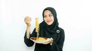 jovem ásia mulher isolado em branco fundo segurando uma prato do Macarrão com garfo e comendo isto foto