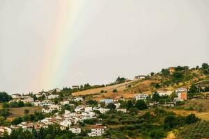 uma arco Iris é visto sobre uma Vila dentro a campo foto