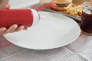 despejando ketchup de garrafa vermelha em um prato branco vazio.