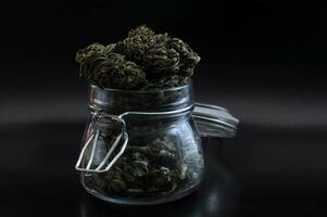 noir ainda vida com vidro pedreiro jarra cheio do seco médico cannabis brotos em Preto fundo foto