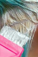cabeleireiro usando Rosa escova enquanto aplicando pintura para fêmea cliente com esmeralda cabelo cor durante processo do branqueamento cabelo raízes foto