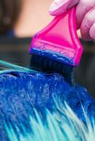 cabeleireiro aplicando azul pintura para fêmea com esmeralda cabelo cor durante processo do tingimento cabelo dentro à moda cor foto