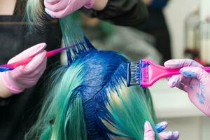 dois profissional cabeleireiro aplicando azul pintura para fêmea com esmeralda cabelo cor durante processo do tingimento cabelo dentro único cor foto