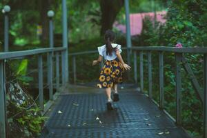 fofa pequeno menina caminhando em uma aço ponte dentro uma botânico jardim com verde plantas e colorida flores em volta. crianças estudando natureza foto