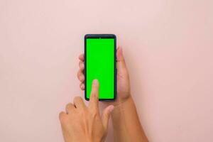 humano mão usando Móvel Smartphone com brincar verde tela em Rosa fundo. masculino mão tocando e pitada para ampliação dentro ou ampliação Fora em em branco digital tela. foto