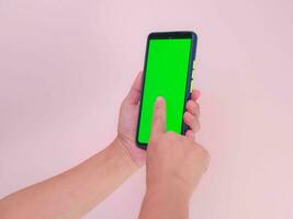 humano mão usando Móvel Smartphone com verde tela isolado em Rosa fundo. mulher mão rolagem alimentação em Smartphone com verde tela brincar. recorte caminho foto