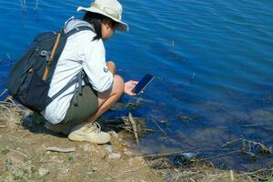 fêmea ecologista usando Móvel telefone para registro análise do patógenos dentro natural águas. água e ecologia conceito foto