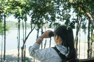 caminhante jovem mulher olhando pássaros através binóculos telescópio dentro floresta. turista com mochila assistindo selvagem pássaros através binóculos dentro a selva. foto