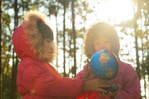 duas lindas garotas asiáticas aprendendo um modelo do mundo no fundo da natureza e luz do sol quente no parque. as crianças aprendem através de atividades lúdicas educativas. Dia da Terra. dia Mundial do Meio Ambiente. foto