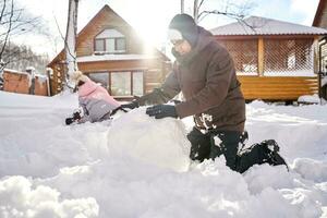 uma família constrói uma boneco de neve Fora do neve dentro a Jardim dentro inverno. foto