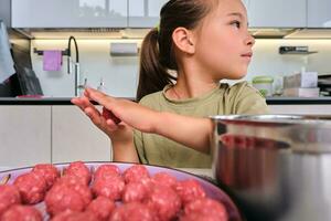 uma menina é preparando almôndegas dentro a cozinha. foto