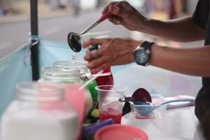 indonésio rua fornecedor mãos preparar uma vidro do beira da estrada fruta gelo Como clientes pacientemente esperar para seus ordens. foto