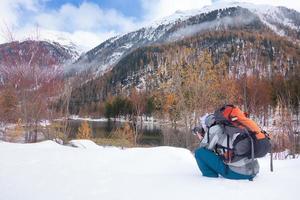 fotógrafo na neve no outono em frente a um lago na montanha foto