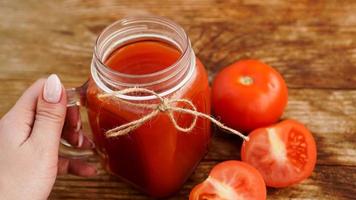 mão feminina segurando um copo de suco de tomate na mesa de madeira foto