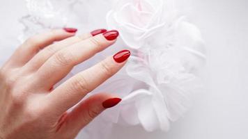 linda mão feminina com unhas vermelhas contra buquê de casamento foto