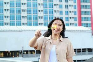 feliz ásia jovem mulher segurando estrelinhas comemoro Novo ano véspera dentro ao ar livre cobertura topo com cidade construção fundo foto