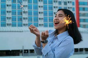 feliz ásia jovem o negócio mulher segurando estrelinhas para comemoro Novo ano véspera em pé dentro ao ar livre cobertura topo com cidade construção fundo foto