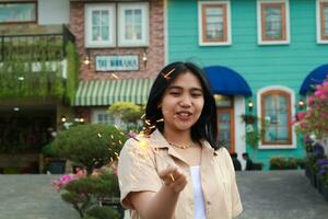 retrato do lindo feliz jovem ásia mulher segurando estrelinhas fogos de artifício para comemoro Novo ano véspera com jardim festa em pé dentro ao ar livre vintage casa Jardim foto