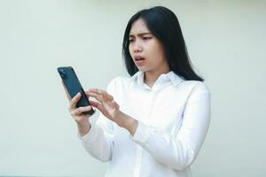 retrato do chocado ásia o negócio mulher empreendedor tocante Smartphone tela surfar ciberespaço vestindo branco camisa formal terno, navegando social meios de comunicação usando aplicativos, em pé isolado foto