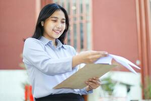 sorridente ásia investimento Gerente Reveja mercado estoque dados dentro papel enquanto caminhando sobre escritório prédio, sucesso vendedora analisando dados vendas vestindo formal terno em pé dentro ao ar livre foto