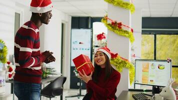 boneca dentro tiro do animado empregado surpreso de carinhoso colega com Natal presente. jubiloso funcionários membro recebendo natal presente às trabalhos dentro escritório decorado com natal luzes e guirlandas foto