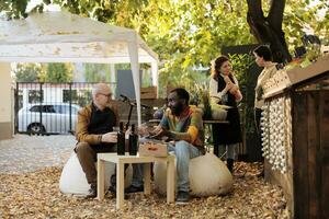 multiétnico equipe do vendedor e cliente degustação caseiro natural vinho, sentado às mesa com enólogo Próximo para agricultores mercado ficar em pé. cliente amostragem local produzir e visitando Comida festival. foto