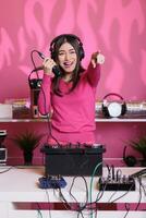 ásia artista realizando eletrônico música usando profissional plataformas giratórias, desfrutando para executar dentro clube às noite. sorridente artista mistura techno som, falando para dentro microfone com fãs foto