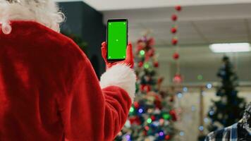 Supervisor dentro natal ornamentado compras Shopping vestindo santa claus terno segurando brincar telefone, lendo promocional Natal ofertas para clientes em verde tela durante inverno feriado temporada, fechar acima foto