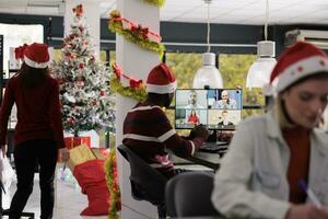 profissional empregado sentado às escrivaninha dentro Natal decorado escritório falando com colegas dentro conectados teleconferência reunião. trabalhador dentro virtual conferência o negócio comunicação escritório ligar foto