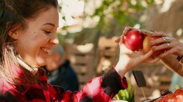 jovem cliente escolhendo colorida maçãs para Comprar a partir de local agricultor, olhando às saudável produtos em mercado verde contador. fêmea cliente visitando agricultores mercado ficar em pé, orgânico produzir. portátil tomada. foto