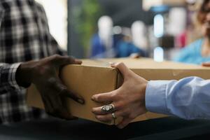 africano americano cliente segurando cartão caixa às contador mesa, depois de comprando elegante mercadoria. à moda homem compras para elegante roupas, discutindo sobre material dentro moderno boutique foto