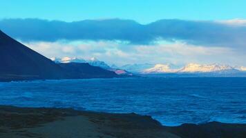 majestoso panorama do Preto areia de praia dentro Islândia, panorâmico Visão do Nevado montanhas e congelando frio águas. lindo islandês cenário em litoral costa com oceano ondas. portátil tomada. foto