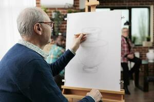 Senior homem sentado às cavalete desenhando vaso com lápis, atendendo social arte Aulas, despertar artístico lado dentro aposentadoria, explorando e descobrindo Novo paixões. maduro aluna praticando desenhando foto