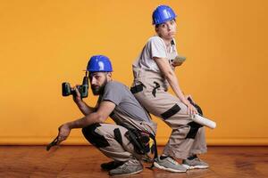 interior construtores agindo confiante com construção ferramentas, posando em estúdio fundo com construção instrumentos. segurando poder broca pistola, par do alicate e pintura escovas. foto