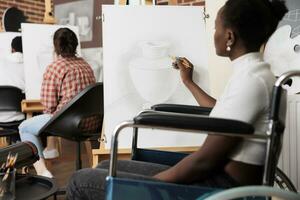 jovem Preto mulher com fisica incapacidade visitando grupo desenhando oficina, criativo terapia para Desativado adultos, arte dentro fisica reabilitação. africano americano menina cadeira de rodas desenhando em tela de pintura foto