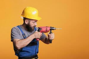 jovem renovando especialista segurando elétrico perfuração arma de fogo para parafuso unhas e trabalhos em construção projeto, em pé sobre estúdio fundo. faz-tudo construtor usando sem fio poder broca ferramenta, carpinteiro. foto