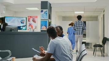 africano americano médico fazendo consulta com homem dentro esperando área às hospital recepção, falando sobre exame resultados e tratamento. geral praticante mostrando notas em médico relatório arquivos. foto