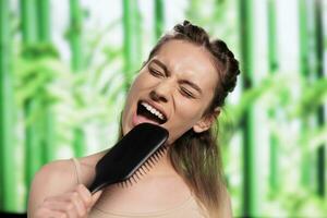 atraente mulher fazendo Penteado e usando escova de cabelo Como microfone. jovem lindo caucasiano senhora ouvindo para música, fingindo para cantar dentro pente e escovar Loiras cabelo foto