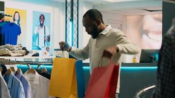 alegre boba homem dançando depois de comprando roupas, levando compras bolsas a partir de dinheiro registro e sentindo-me feliz. jovem brincalhão cliente fazendo dança movimentos agindo engraçado dentro roupas loja. foto