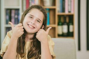 fofa criança pequeno menina caucasiano Castanho cabelo feliz sorridente dois polegares acima gostar para lendo e Educação dentro escola foto