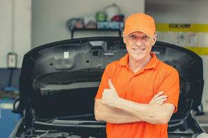 Senior profissional Veja carro mecânico em pé dentro garagem. retrato feliz sorridente caucasiano adulto masculino dentro auto serviço polegares acima. foto